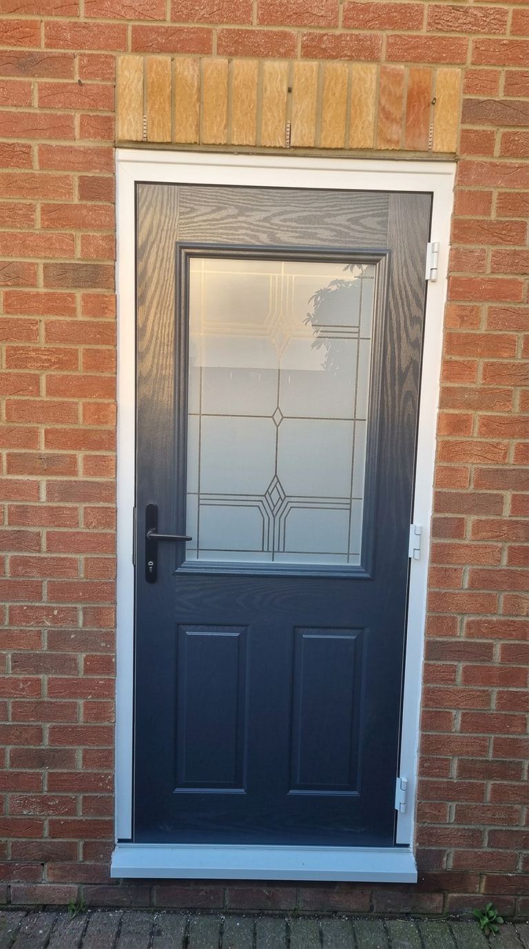 Black composite door with decorative glazed panel in red brick opening