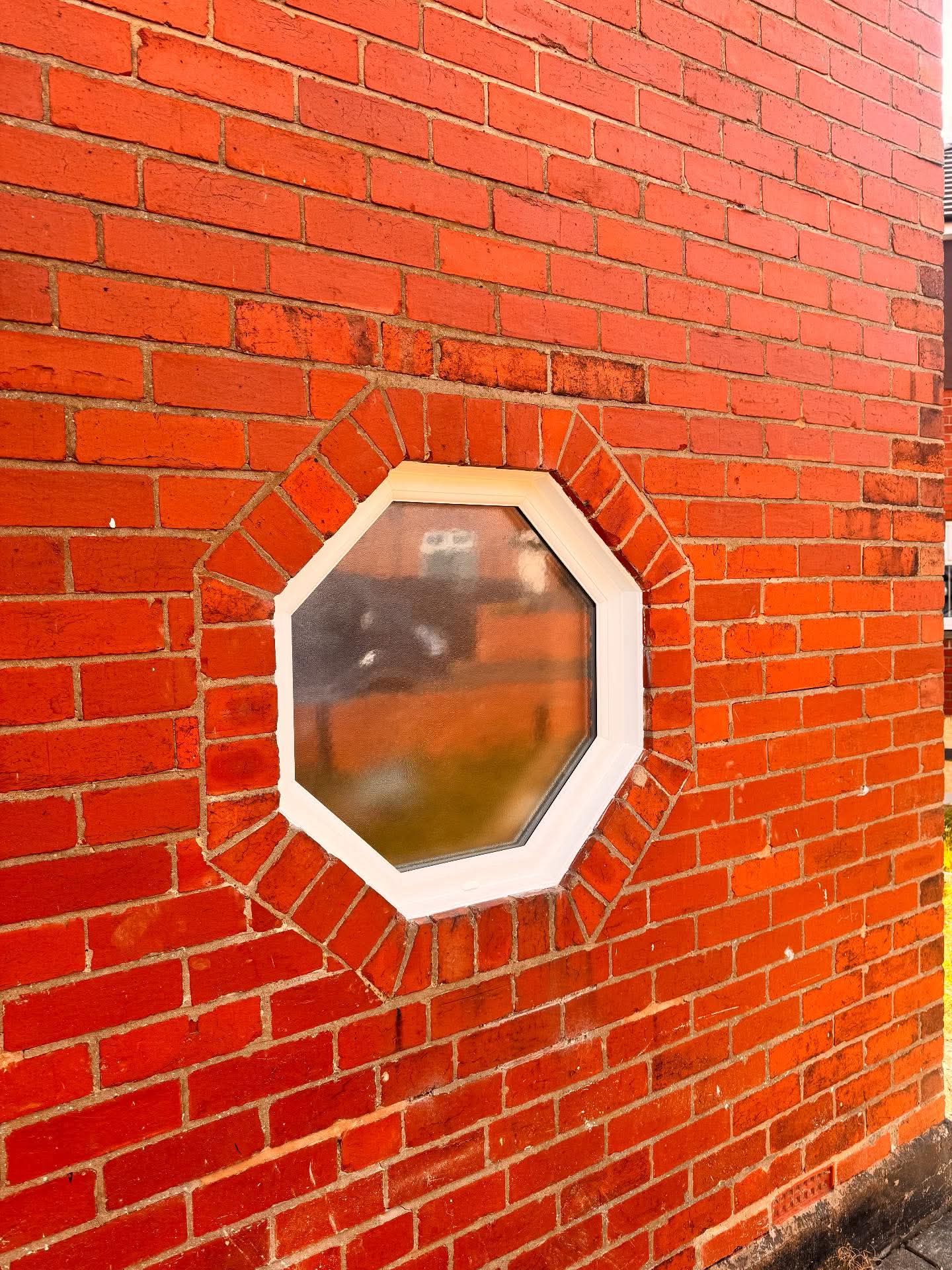 Octagonal white uPVC window in red brick wall
