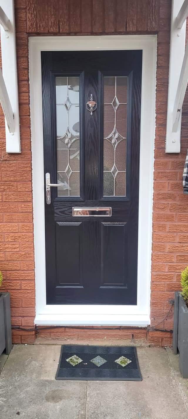 Black composite front door with diamond leaded glass in a red brick porch