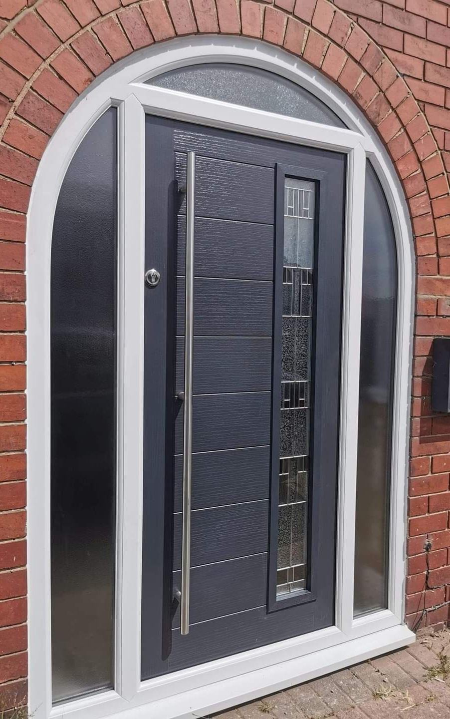 Anthracite grey composite door with sidelight in an arched red brick surround
