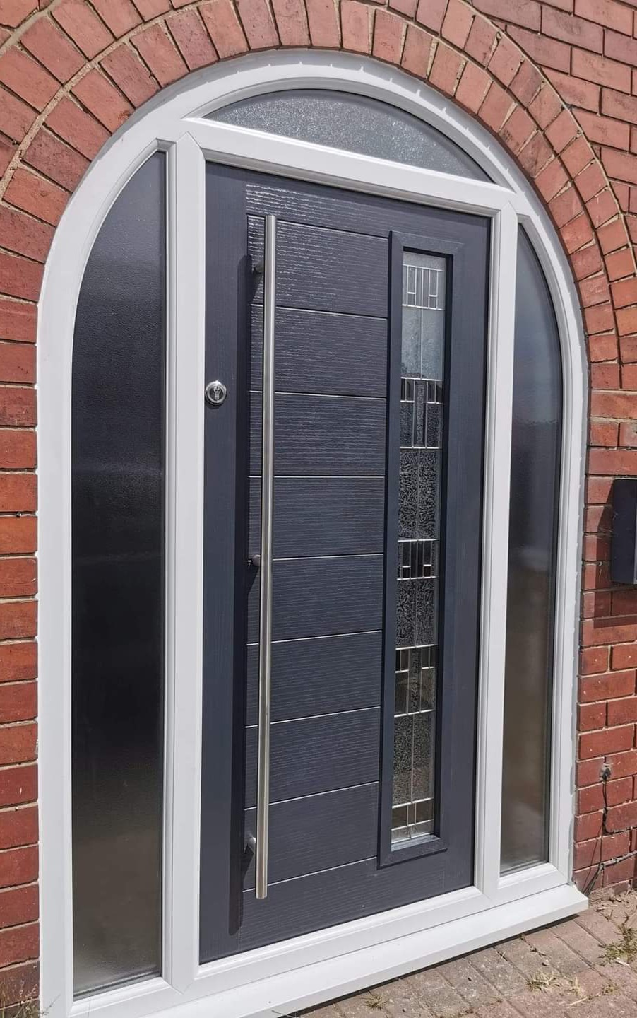Anthracite grey composite door with sidelight in an arched red brick surround