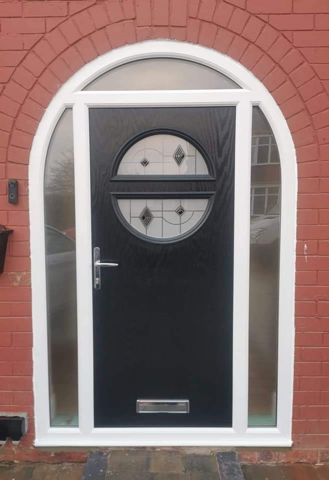 Black composite door with circular glass set in an arched brick surround